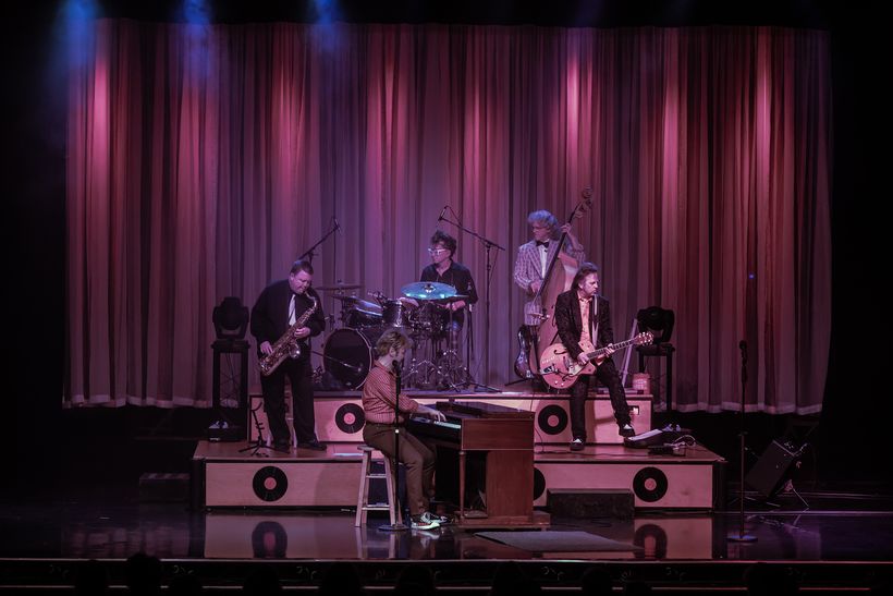 A band on stage in front of red curtains